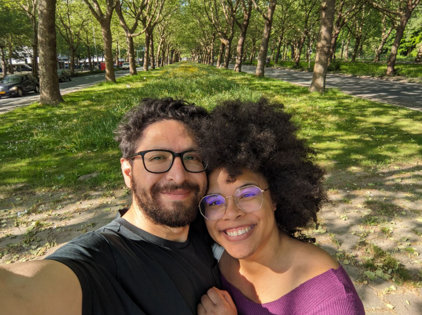 Allan and misha take a selfie with a corridor of tree-lined grass behind them.